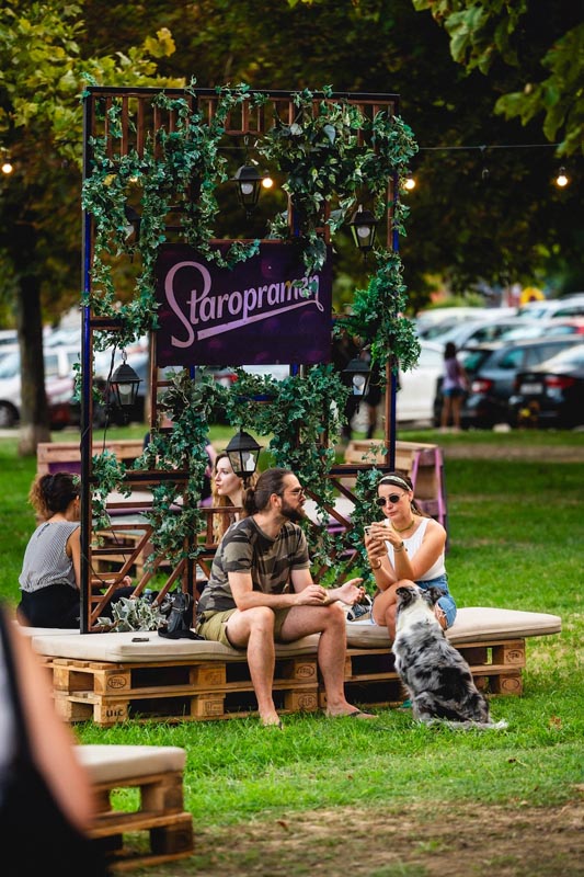 Posjetitelji Staropramen chill zone u parku sjede na drvenim paletama u pratnji psa.