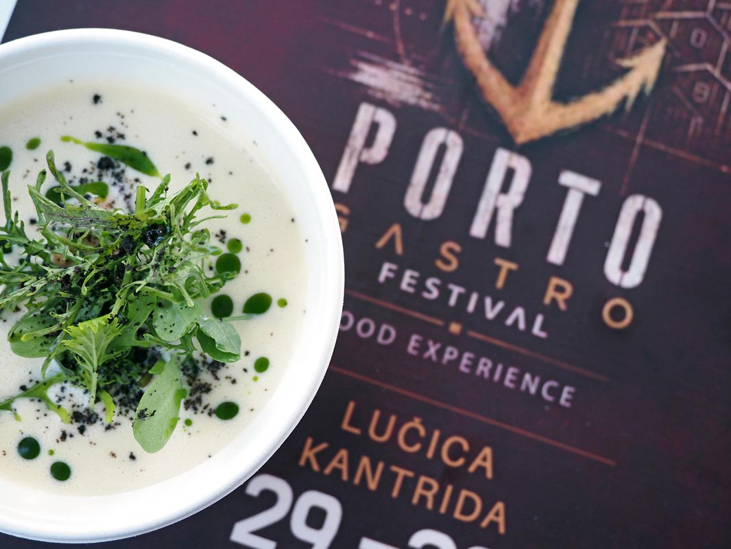 P8291204 Krem juha dekorirana zelenim uljem i svježim klicama pored Porto Gastro Festival plakata.
