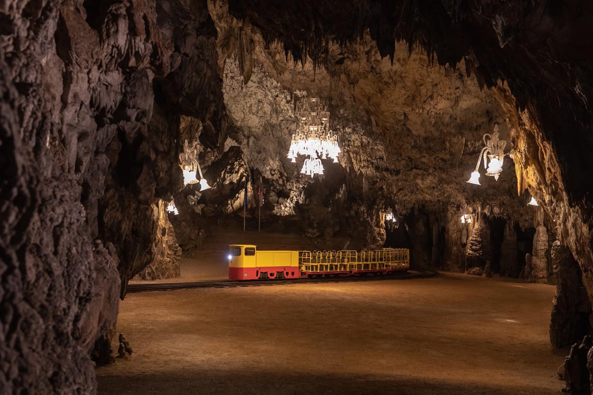 Žuto-crveni vlakić na tračnicama ispod raskošnog lustera u dvorani Postojnske jame