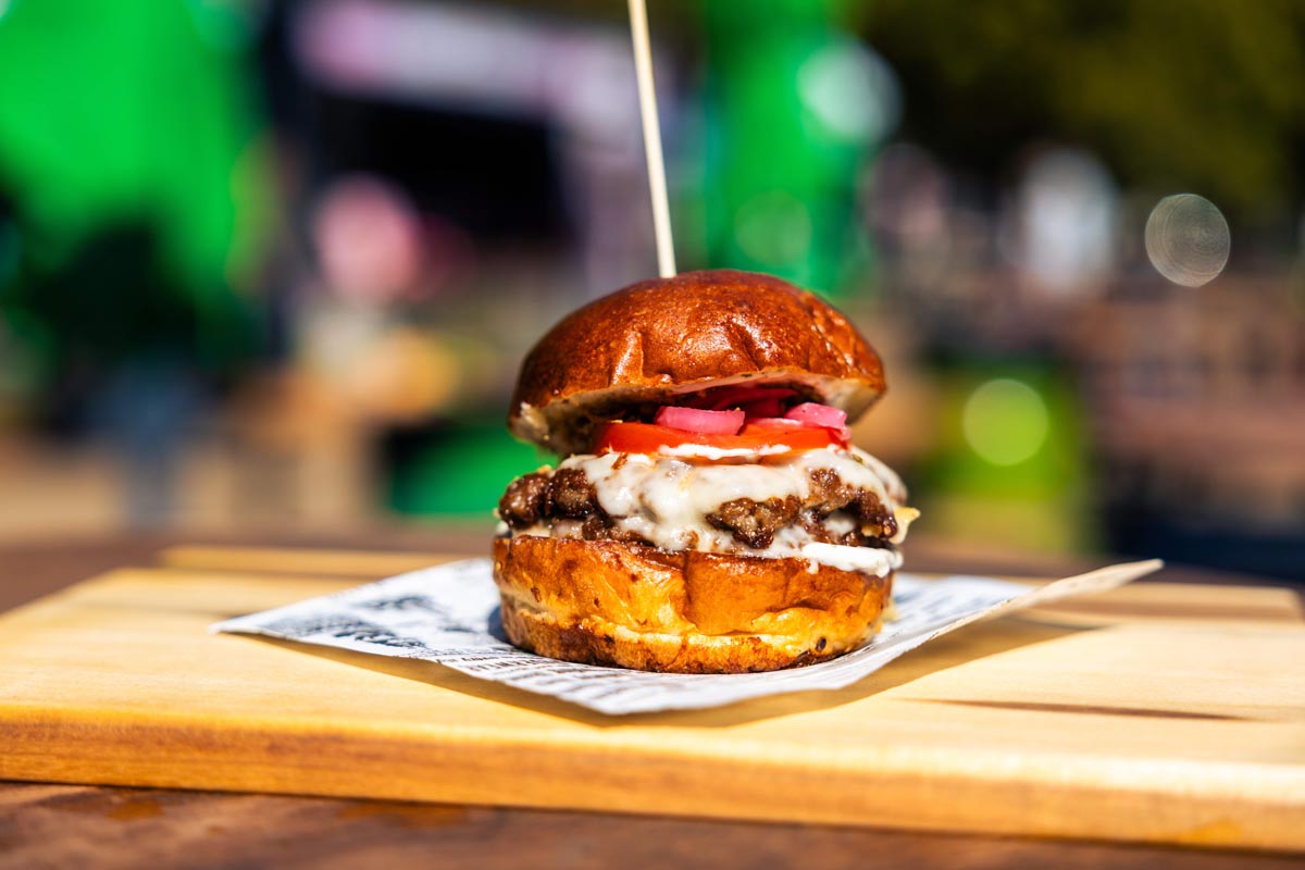 Gourmet burger s topljenim sirom, rajčicom i ukiseljenim lukom proboden drvenim štapićem