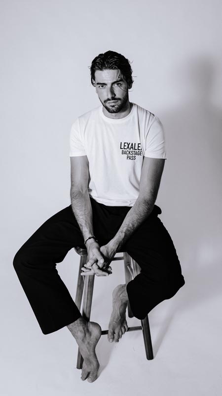 Muška bijela majica Lexalex Backstage Pass i crne hlače u ležernoj studijskoj kombinaciji.