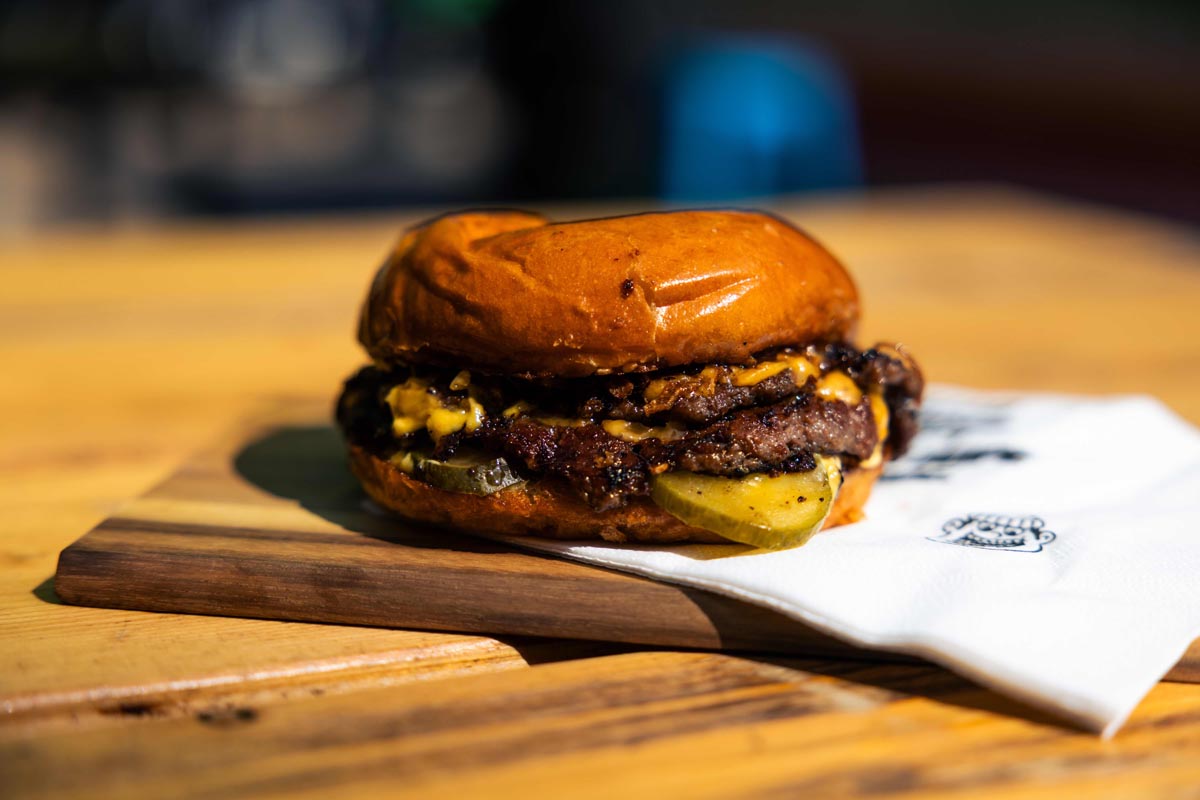 Sočni smash burger s rastopljenim sirom i kiselim krastavcima na drvenoj podlozi