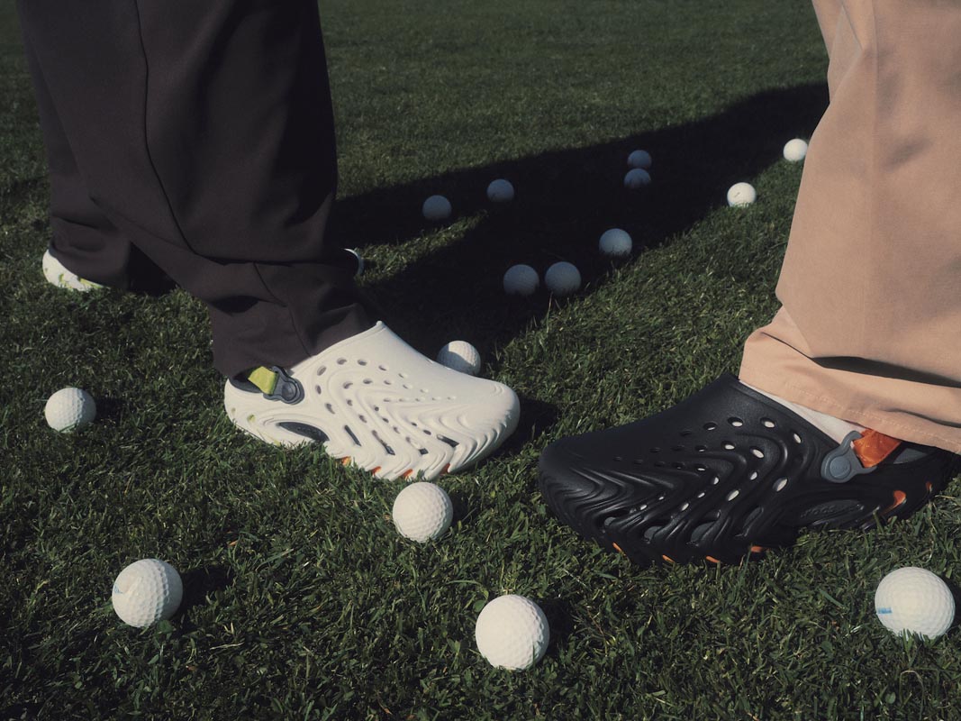 Bijele i crne muške natikače Crocs Echo II na nogama modela na travnatom golf terenu s lopticama.