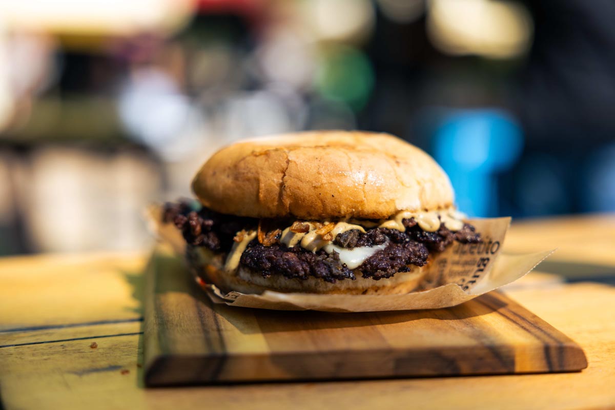 Hrskavi burger s umakom i prženim lukom poslužen na papiru i drvenom poslužavniku