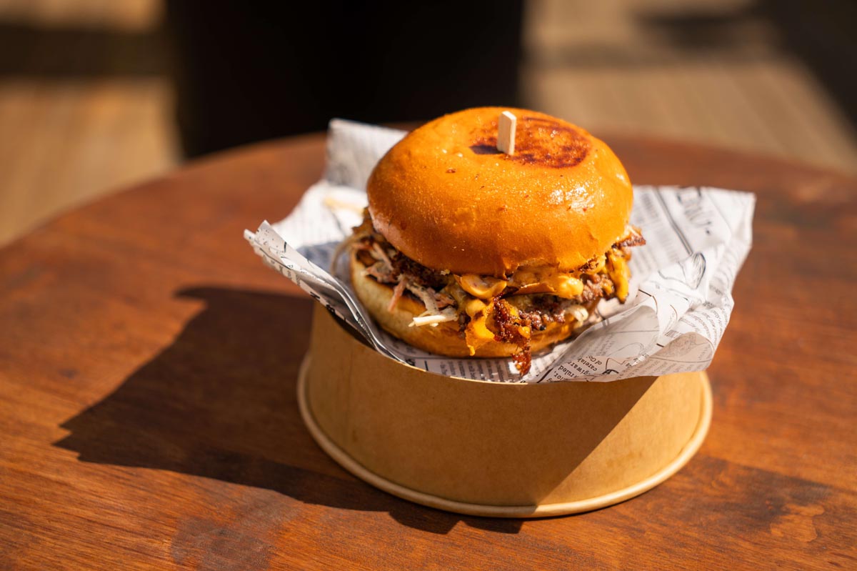 Burger s topljenim sirom i coleslaw salatom poslužen na okrugloj papirnatoj posudi