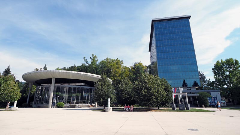 Trg ispred modernog staklenog tornja i kružnog paviljona Medical Center Rogaška u Sloveniji pod plavim nebom.