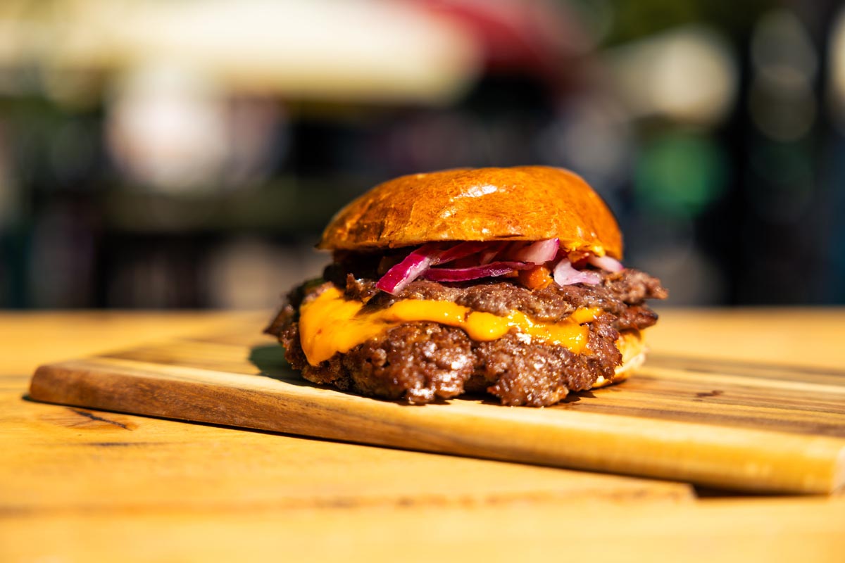 Dvostruki smash burger s rastopljenim cheddar sirom i ljubičastim lukom na drvenoj dasci