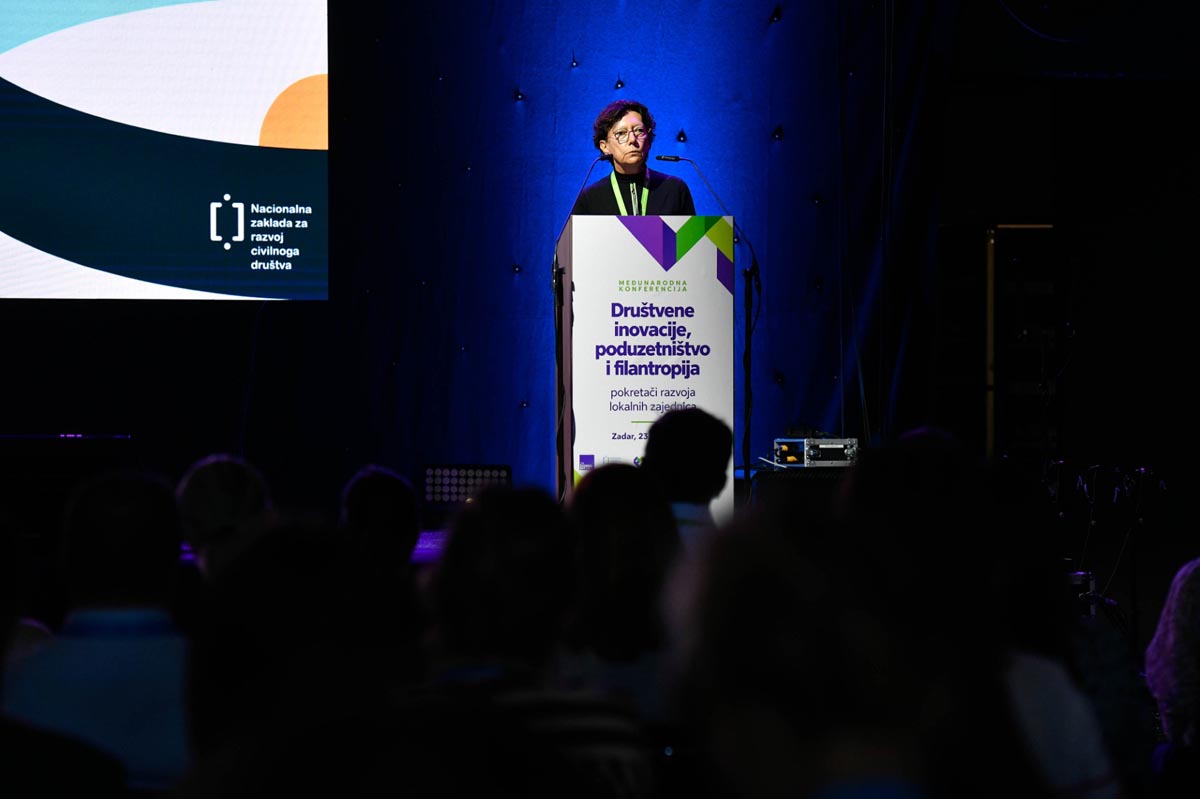 Govornica za pultom konferencije Društvene inovacije, poduzetništvo i filantropija pred publikom u zamračenoj dvorani