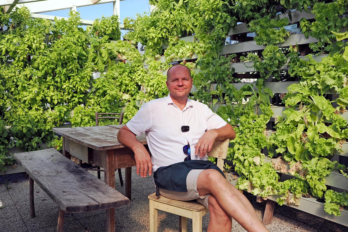 Tourist-farm-Pomona-31 Vlasnik Janko Zupanec sjedi za drvenim stolom ispred bujnog vertikalnog vrta na eko imanju Pomona Turizem na podeželju.