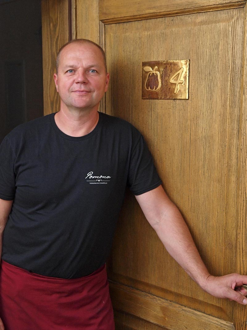 Janko Zupanec u crnoj majici i bordo pregači ispred drvenih vrata hotelske sobe na turističkom seoskom gospodarstvu Pomona.