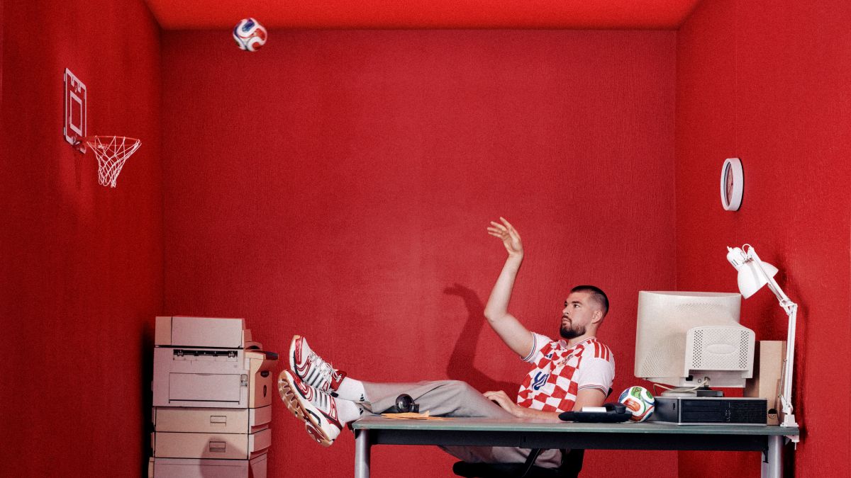 Košarkaš Ivica Zubac u hrvatskom dresu sjedi za radnim stolom i baca loptu prema mini košu