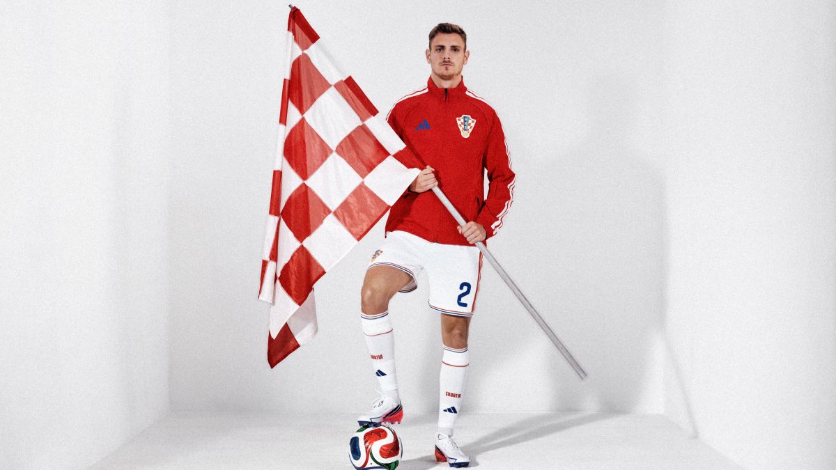 rvatski nogometaš Josip Stanišić u crvenoj sportskoj jakni drži veliku kockastu zastavu