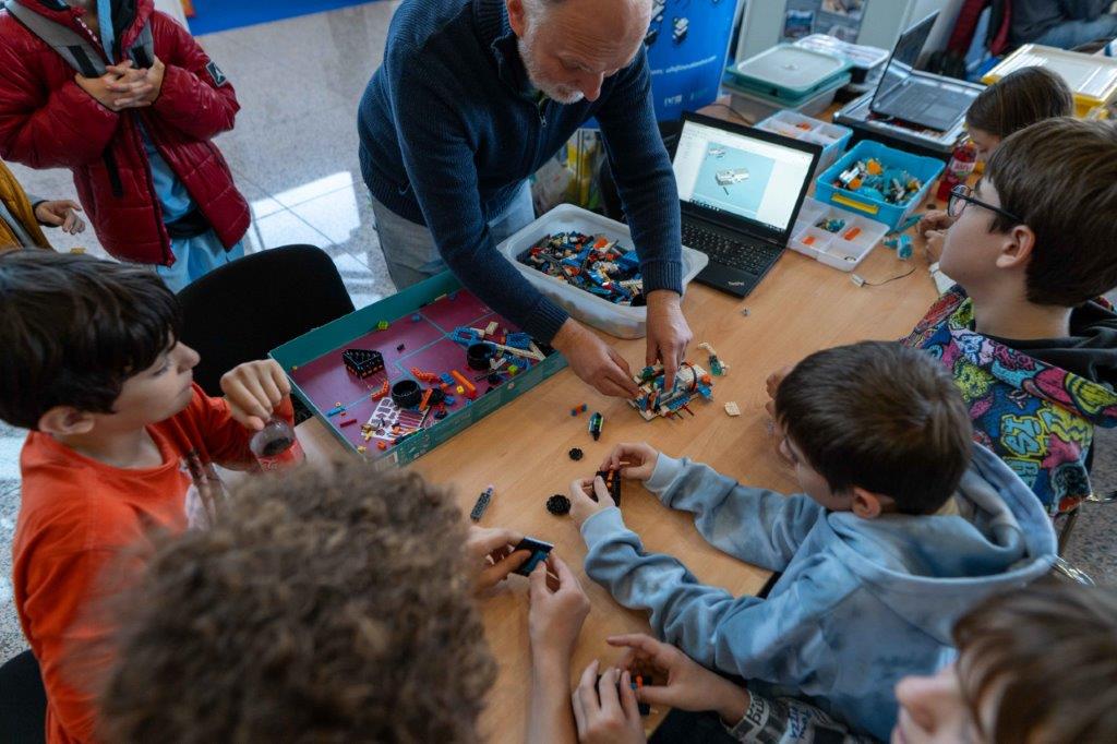 Mentor pomaže djeci u slaganju Lego robota pomoću laptopa i nacrta na radionici robotike tijekom sajma ARCA