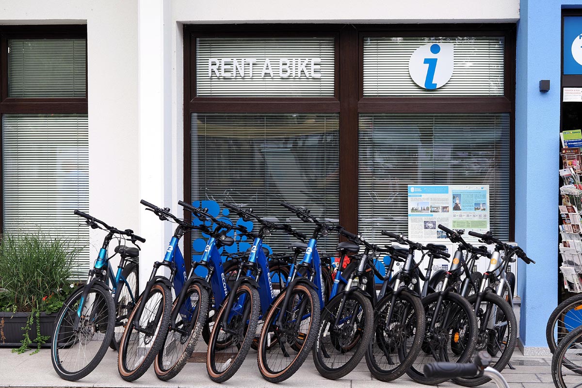 Plavi i crni bicikli poredani ispred ureda s natpisom Rent a bike i oznakom info centra