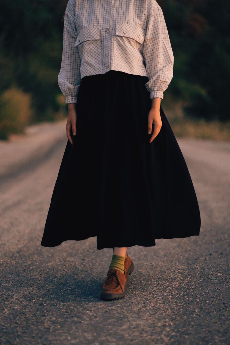 Ženski retro outfit s dugom crnom maksi suknjom, kariranom košuljom i smeđim antilop cipelama