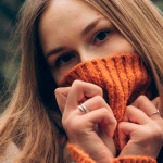Djevojka s dugom kosom pokrila je usta pletenim narančastim puloverom