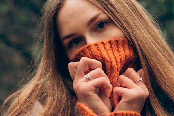 Djevojka s dugom kosom pokrila je usta pletenim narančastim puloverom