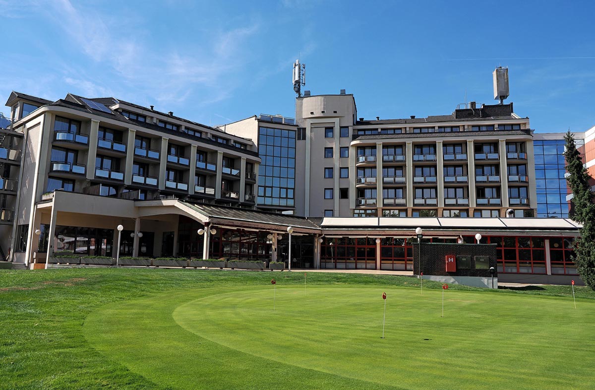Pogled na zgradu hotela Ajda s brojnim balkonima i staklenim stijenama iza golf igrališta