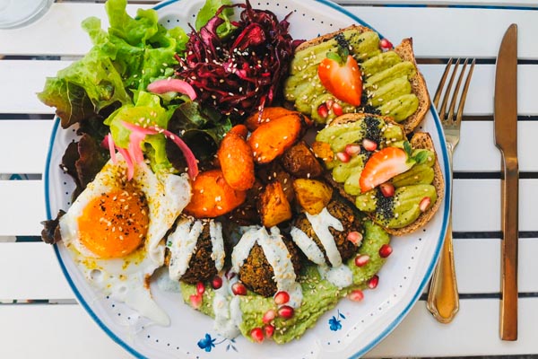 Bogata zdjela za doručak s jajima na oko, falafelom, pečenim povrćem i tostom s avokadom
