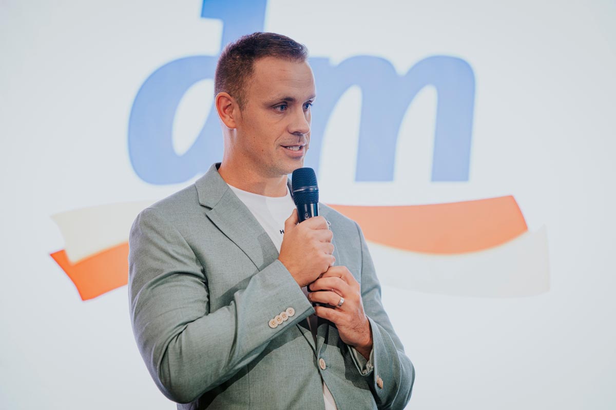 Ivan Horvat u sivom sakou govori na mikrofon ispred velikog dm logotipa u pozadini