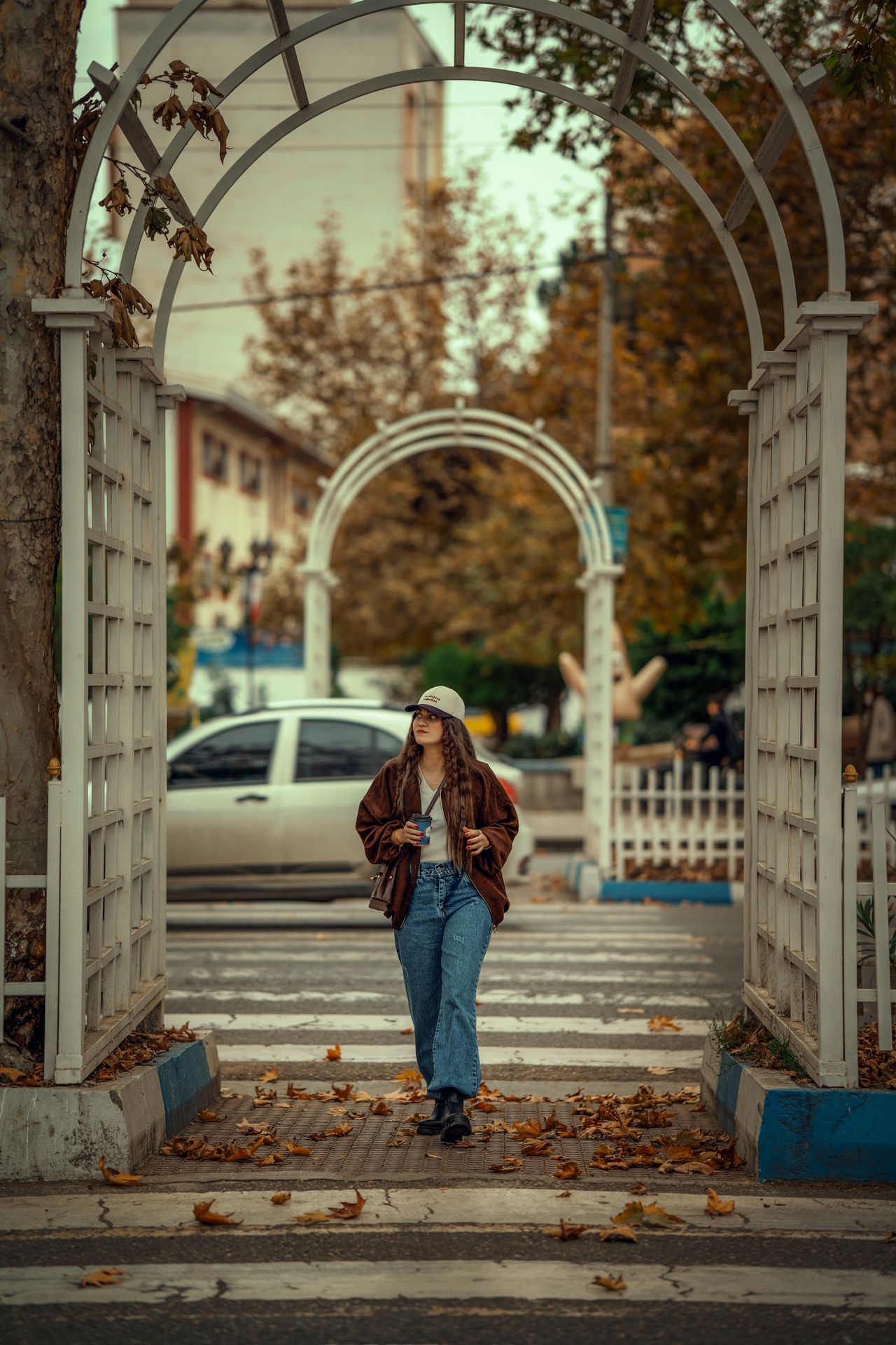 Žena u trapericama i sa šiltericom prolazi ispod drvenog luka u gradskom parku
