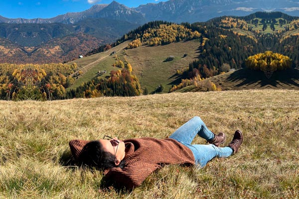 Žena se odmara na planinskom pašnjaku okružena žutim šumama i brdima pod suncem