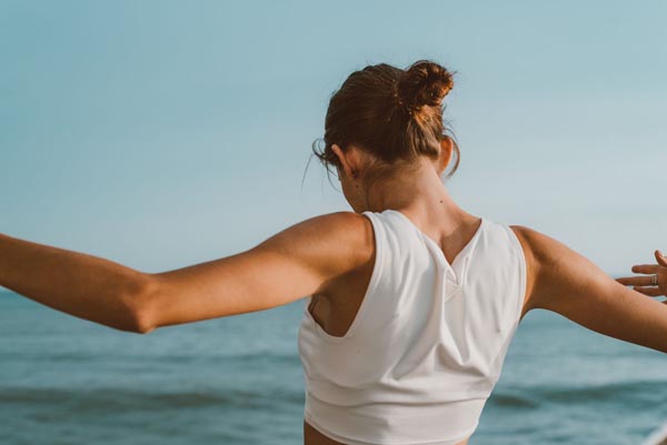 Žena radi vježbe istezanja ili jogu na otvorenome uz more s pogledom na plavo nebo.