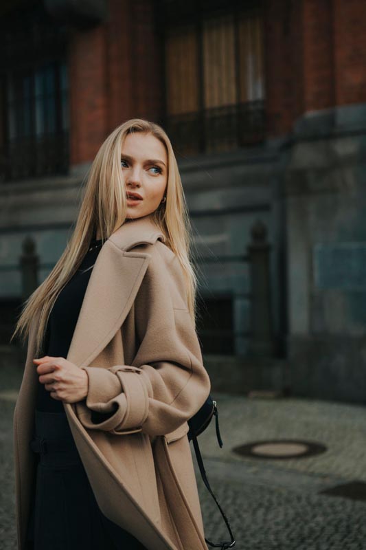 Plavokosa žena u elegantnom smeđem kaputu gleda u stranu na ulici
