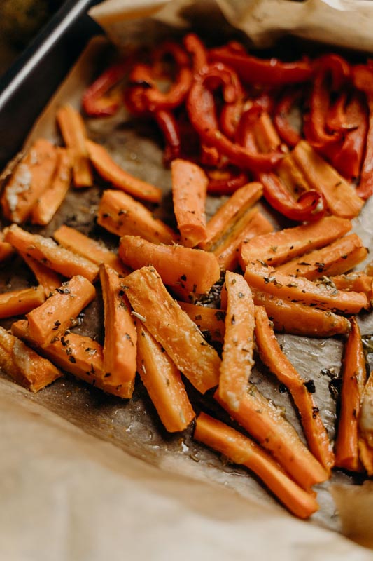 Pečena mrkva narezana na štapiće i crvena paprika na papiru za pečenje u protvanu