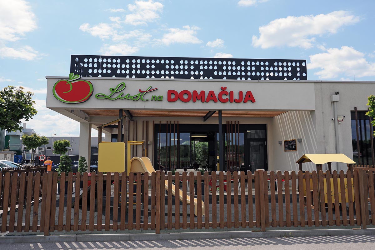 Moderni prodajni objekt Luštna domačija s drvenom ogradom i dječjim igralištem ispred ulaza