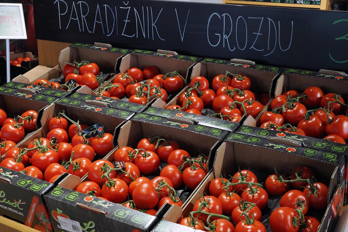 Kutije pune Lušt rajčica u grozdu poslagane na polici ispod ploče s natpisom paradižnik v grozdu