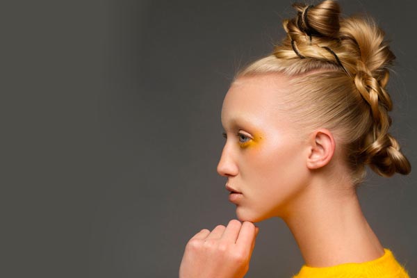 Žena iz profila s kreativnom pletenicom na vrhu glave i žutim sjenilom na očima