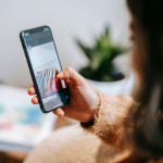 Žena na pametnom telefonu gleda fotografiju odjeće obješene na vješalice