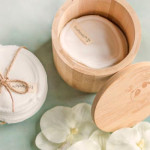 Pogled odozgo na perive jastučiće za čišćenje lica vezane špagom pokraj otvorene bambusove posude i cvijeća