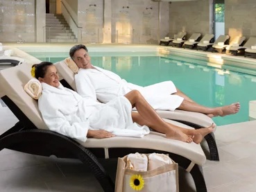 wellness-livada-prestige Par u bijelim ogrtačima opušta se na ležaljkama pokraj unutarnjeg bazena u wellness centru hotela Livada Prestige.