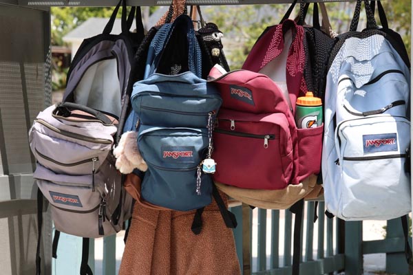 Četiri ruksaka marke JanSport u različitim bojama vise obješeni na metalnoj konstrukciji na otvorenom.