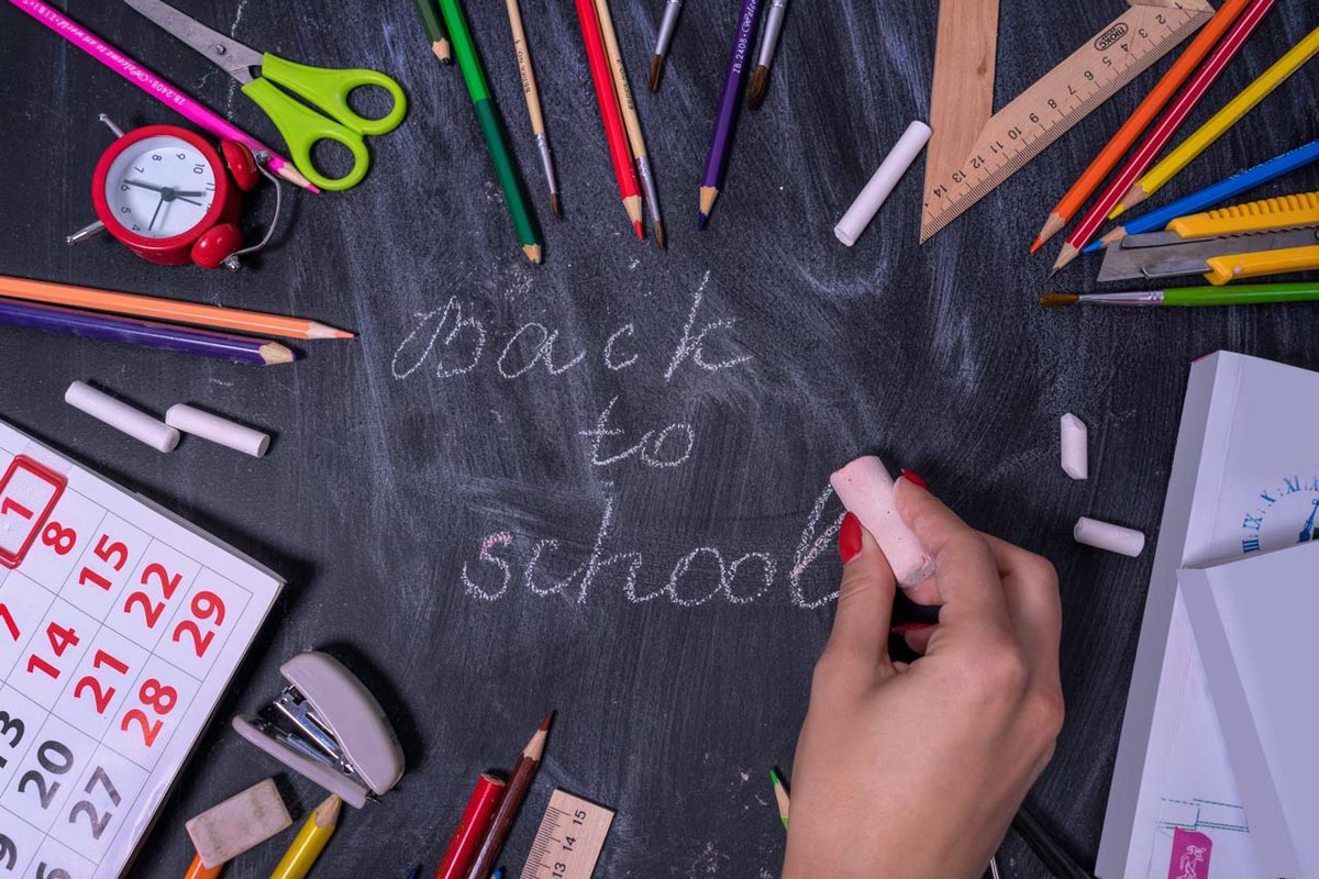 Školski pribor i kalendar poslagani oko natpisa Back to school napisanog kredom na crnoj ploči.