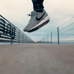 Sive Nike Air sportske tenisice u zraku tijekom skoka na modernoj šetnici.