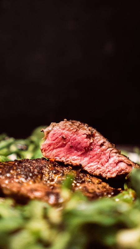 steak_u_restoranu_2 Krupni plan medium-rare pečenog bifteka narezanog na komade na podlozi od zelene salate s tamnom pozadinom