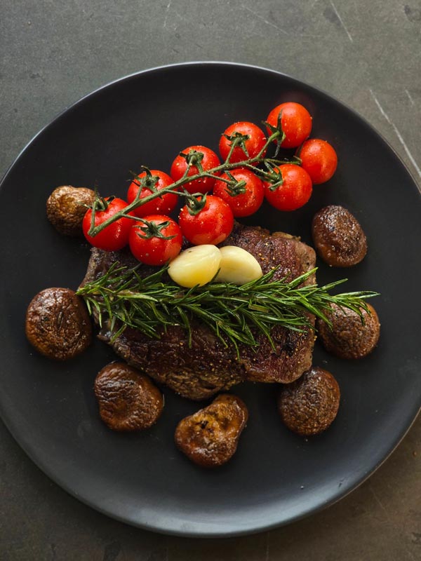 steak_u_restoranu_3 Sočni ramstek s grillanim šampinjonima, češnjakom i grančicom svježeg ružmarina na tamnoj podlozi
