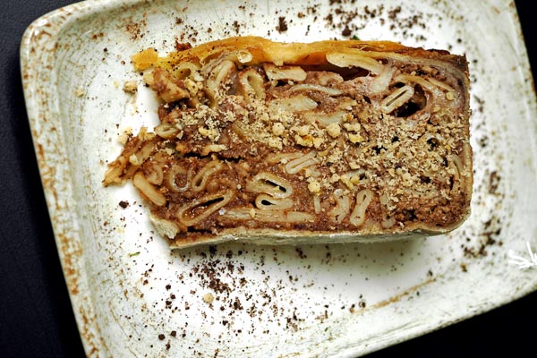 Krupni plan kriške stonske torte koji prikazuje slojeve tankog prhkog tijesta i bogatog nadjeva od tjestenine i čokolade.