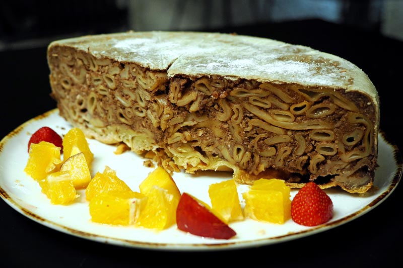 Polovica tradicionalne stonske torte od makarona, badema i čokolade, poslužena s narezanim narančama i jagodama na tanjuru.