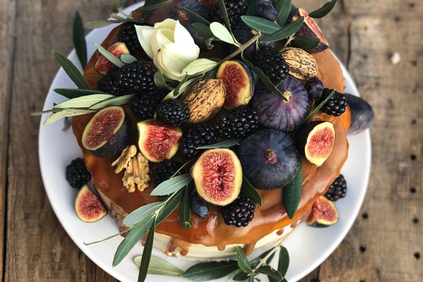 Domaća torta s preljevom od karamele ukrašena smokvama, kupinama, orasima i grančicama masline.
