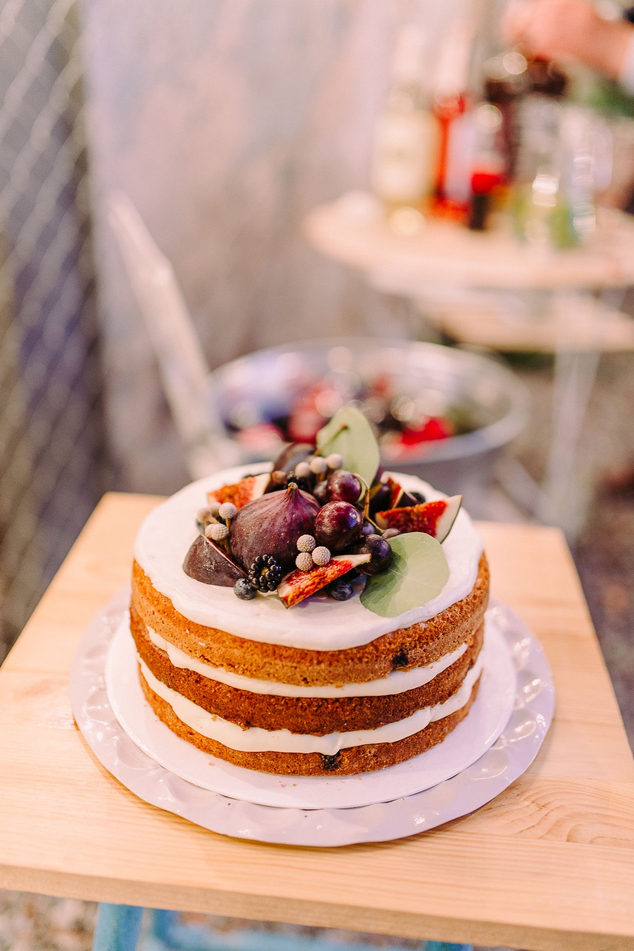 Naked torta s bijelom kremom ukrašena svježim smokvama, kupinama i grožđem na drvenom stalku.