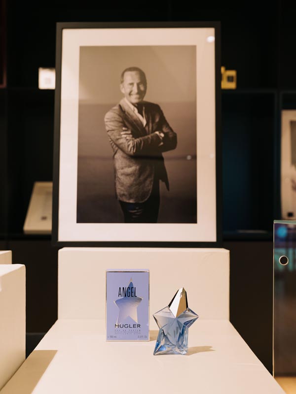 Bočica i kutija parfema Mugler Angel ispred uokvirenog portreta dizajnera Thierryja Muglera