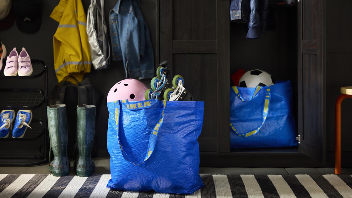 Plava IKEA FRAKTA torba s rošulama i ružičastom kacigom u predsoblju pokraj tamnog ormara za odjeću