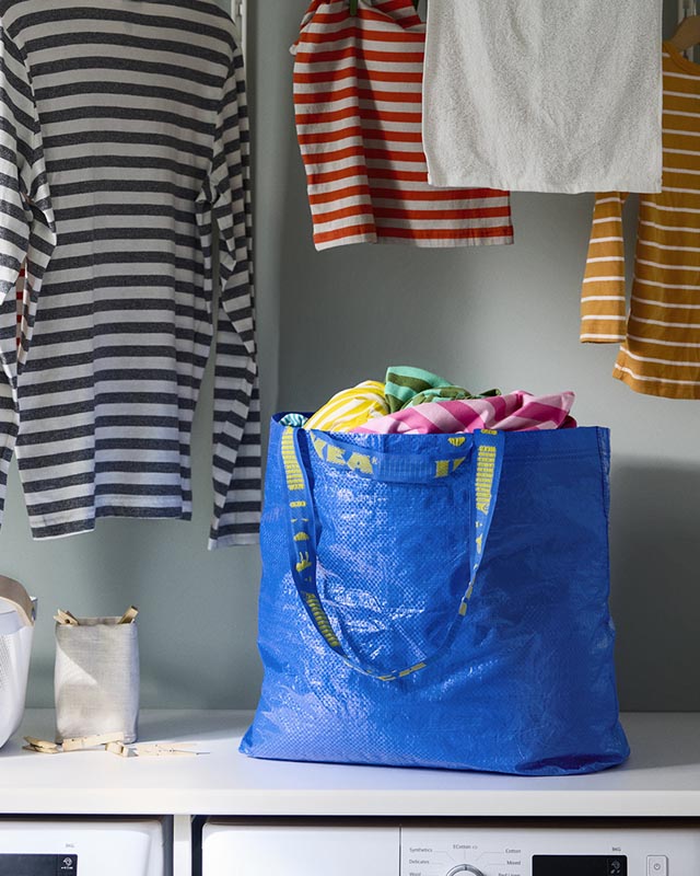 Velika plava IKEA FRAKTA torba puna šarenog rublja stoji u praonici pokraj perilice i obješenih majica