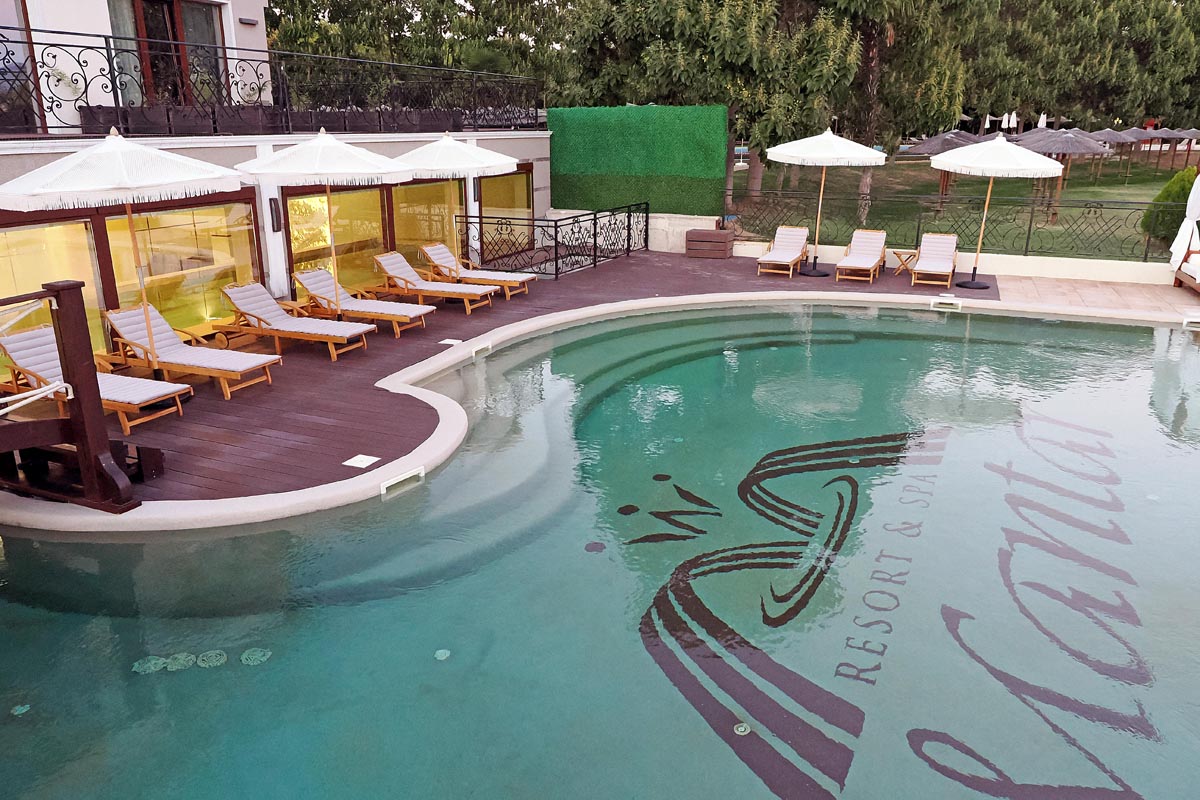 Vanjski bazen hotela Mantar Resort i Spa s logotipom na dnu, ležaljkama i bijelim suncobranima