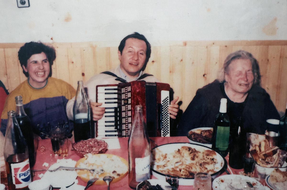 Arhivska fotografija Babe Vange za stolom s harmonikašem i gostima tijekom proslave uz hranu i piće