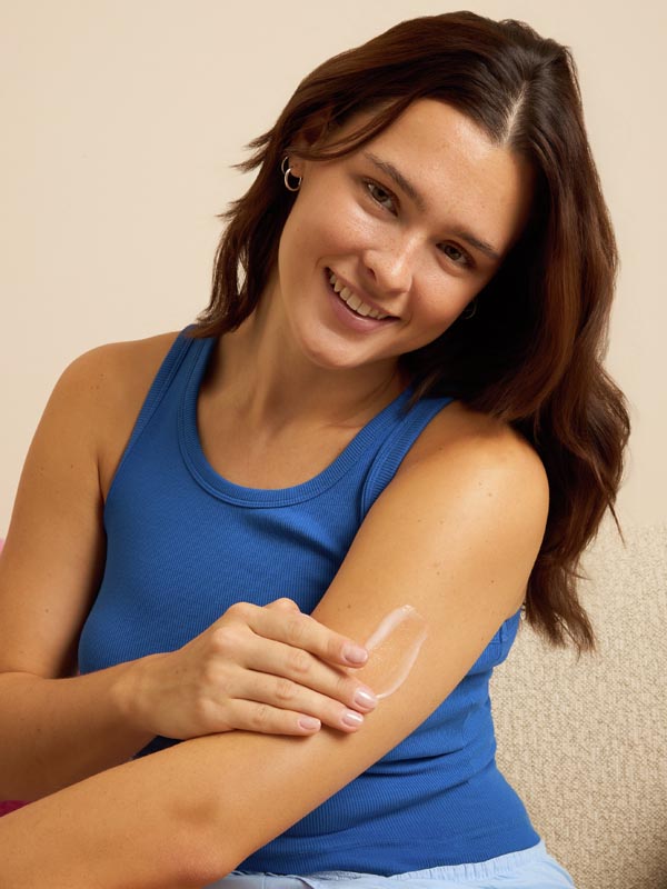 Nasmijana djevojka u plavoj majici nanosi lagani Nivea serum losion za tijelo na nadlakticu